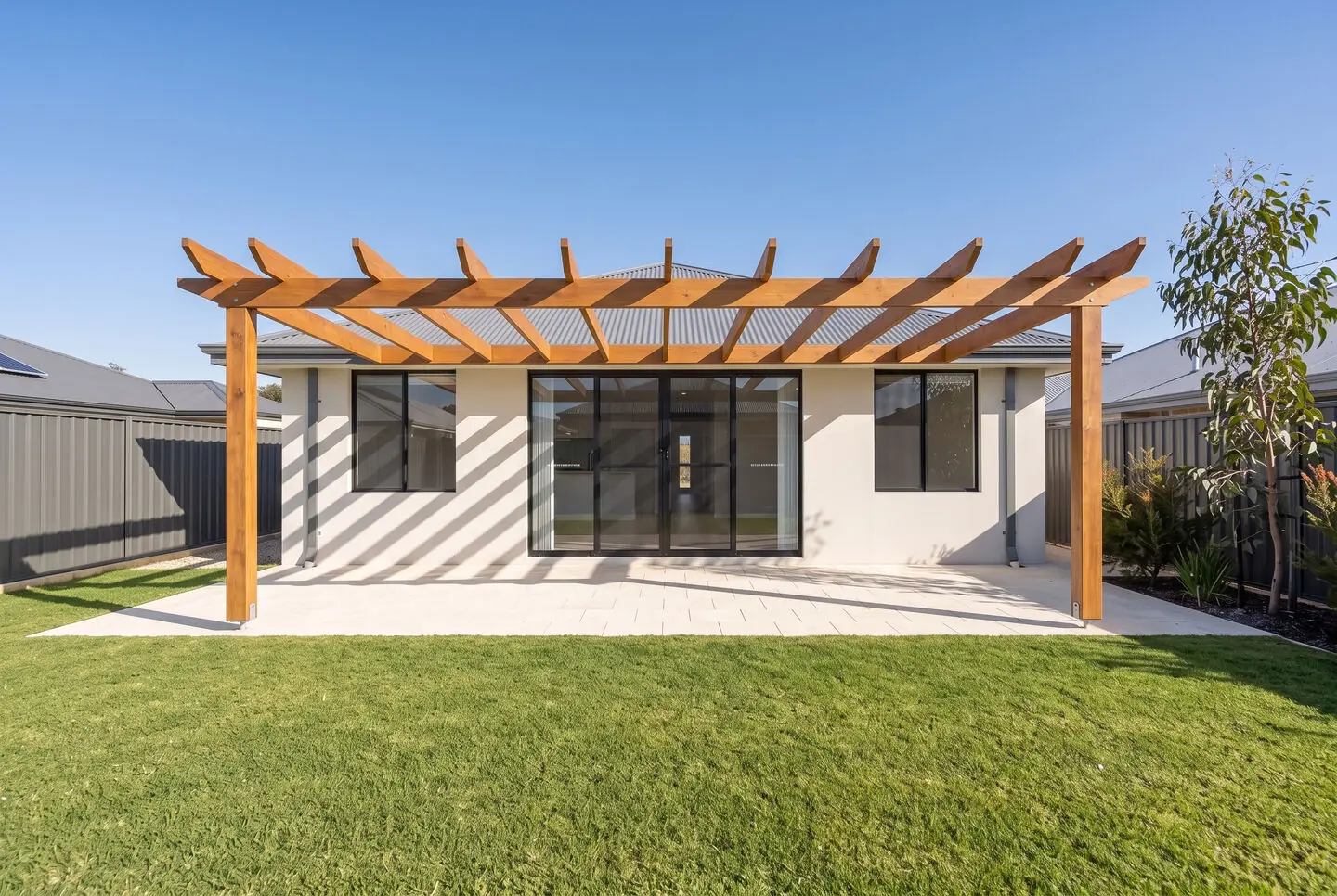 Open timber pergola casting striped shade over limestone paving
